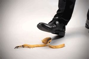 slip-and-fall: photo of man's foot in black shoe and black dress pants hovering over banana peel