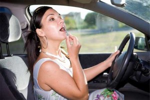 Distracted driver: photo of woman behind wheel of car applying lipstick in rear view mirror