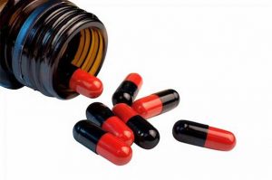 Photo of top of open brown medicine bottle with black and red capsules spilling out