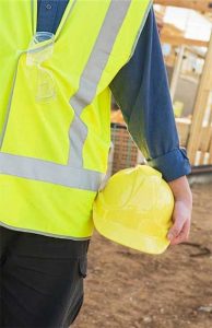 Workplace safety - photo of worker at building site wearing yellow reflective vest and holding yellow hardhat