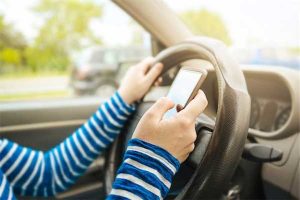 Distracted driving photo of arms of driver with one hand on steering wheel and the other operating a cell phone