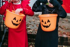 Orange jack-o-lantern buckets with Halloween candy held by children in costumes.