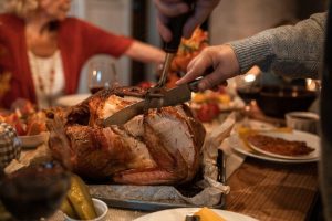 Man carving turkey at Thanksgiving table. Tips for avoiding Holiday accidents.