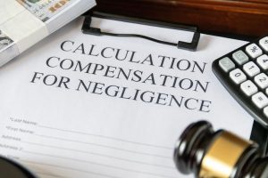 Clipboard holding negligence compensation calculation form with budle of cash and gavel -- Personal Injury compensation is determined according to applicable negligence rule